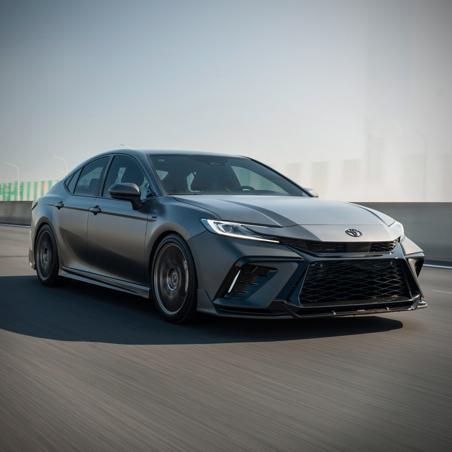 Silver 2025-2026 Toyota Camry with the YOFER front bumper in motion
on a highway, driver-side three-quarter view showing the front splitter