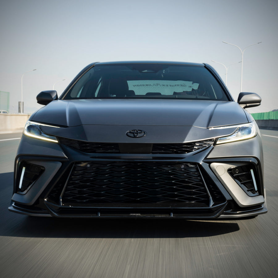 Head-on view of a silver 2025-2026 Toyota Camry in motion with the YOFER
front bumper, LED daytime running lights illuminated in both corner intakes
